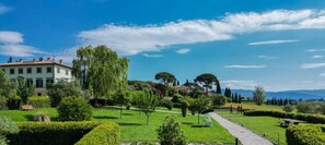 Ein gepflegter Garten mit einem Weg, ein Gebäude mit einem Ziegeldach und in der Ferne Berge.