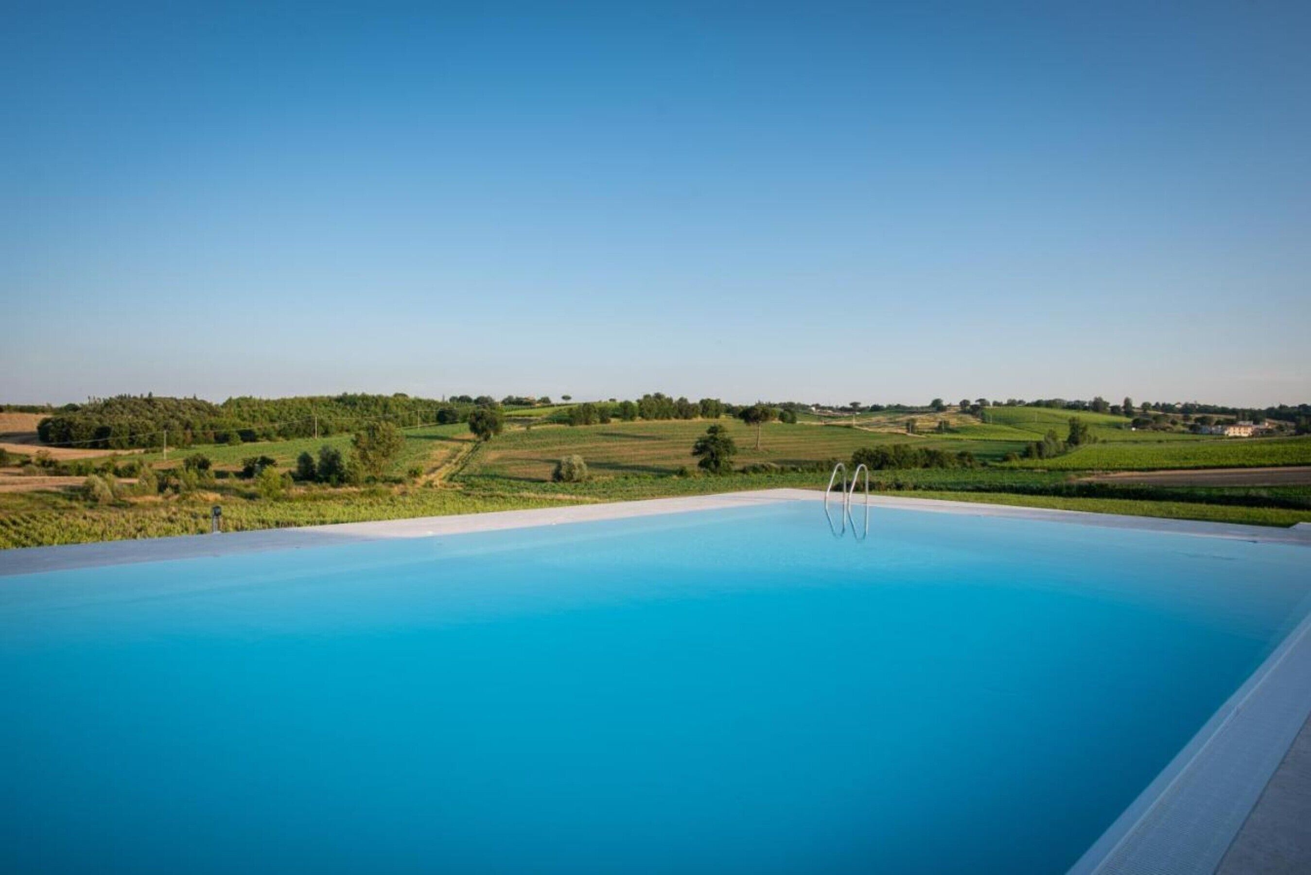 A clear blue swimming pool with a view of green fields and distant hills.