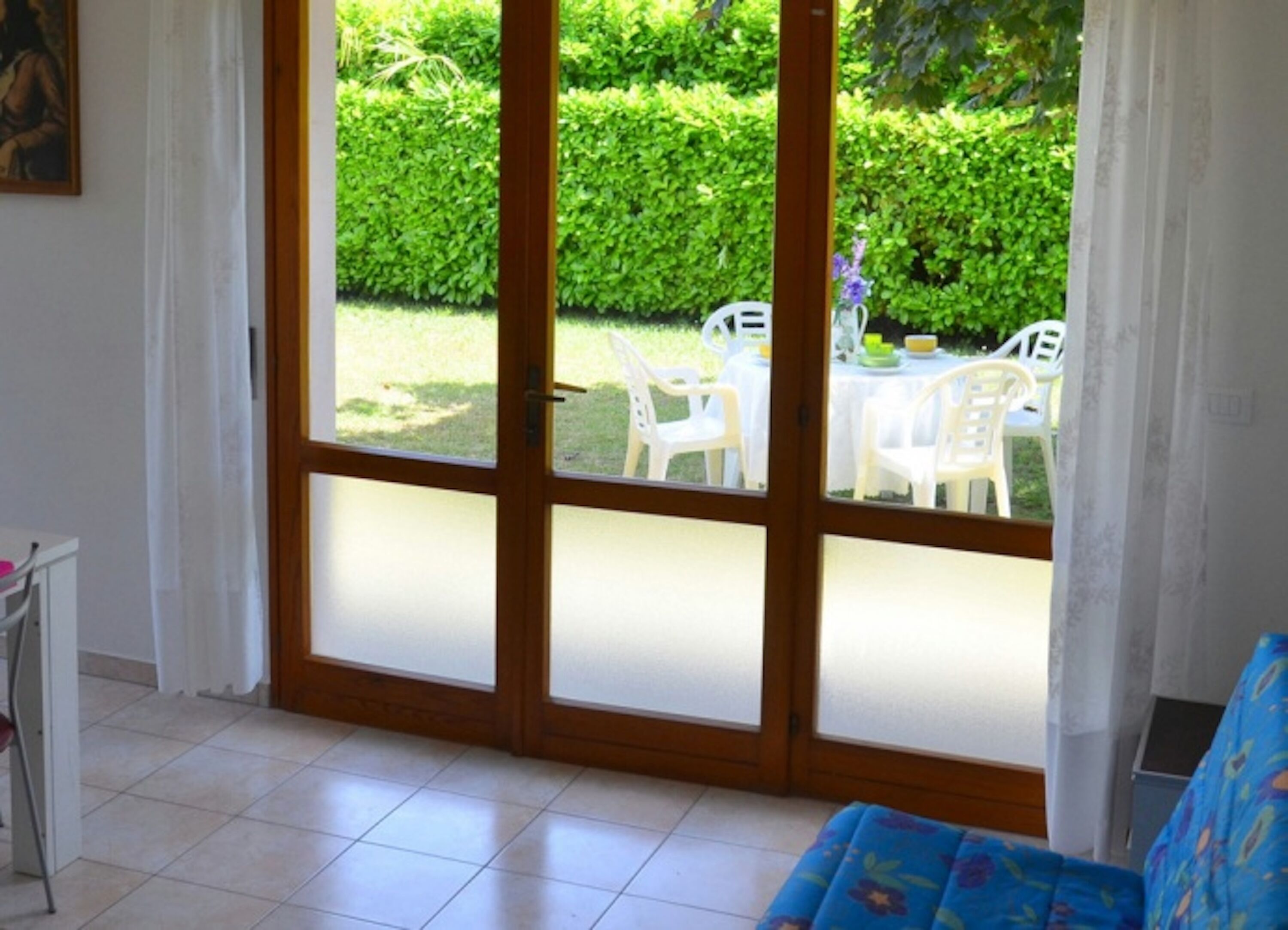 A room with a large sliding glass door leading to an outdoor area with white plastic chairs and a table.