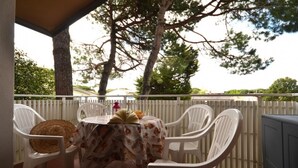 A covered patio with white plastic chairs and a table, surrounded by a white fence and trees.