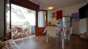 A dining area with a table set for four, a sofa, and a kitchen with a refrigerator and cabinets.