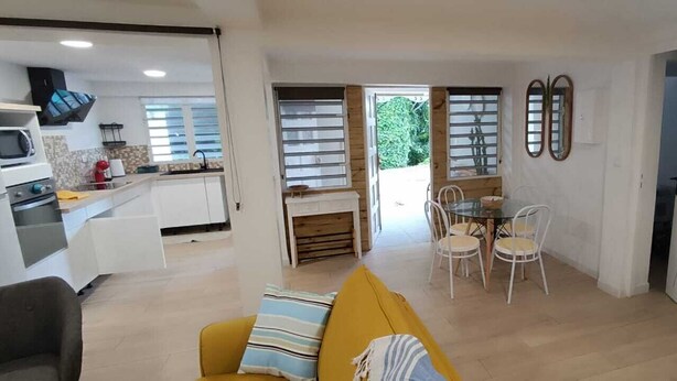 Una cocina moderna con armarios blancos, un microondas y una estufa. Hay un comedor con una mesa y sillas, y un sofá amarillo en primer plano.