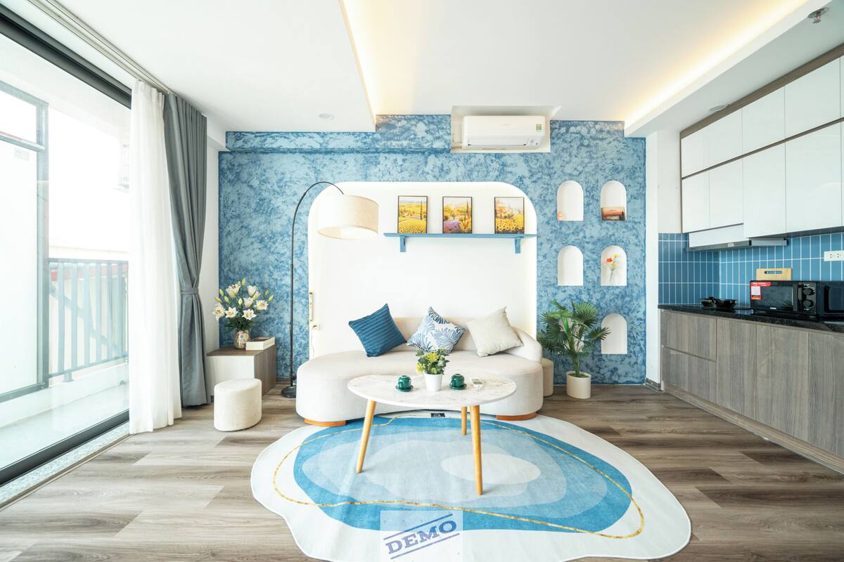 A modern living room with a sofa, coffee table, and decorative items. There is a kitchen area with cabinets and appliances.