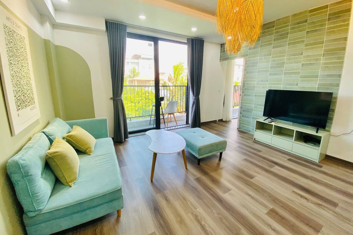A modern living room with a sofa, ottoman, and a flat-screen TV on a stand.