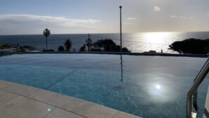 Una piscina trasparente con vista sull'oceano e un tramonto.