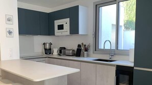 Una cucina moderna con un piano di lavoro bianco, mobili grigi, un forno a microonde integrato e una finestra che offre luce naturale.