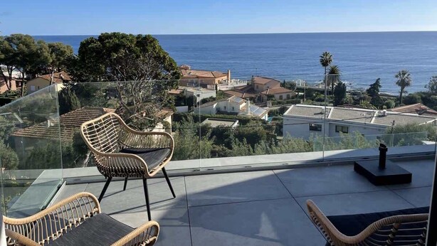 Un balcone con sedie in vimini e vista sul mare e sugli edifici.