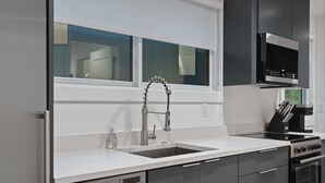 Una cocina moderna con un lavamanos de acero inoxidable, horno empotrado y campana extractora negra.