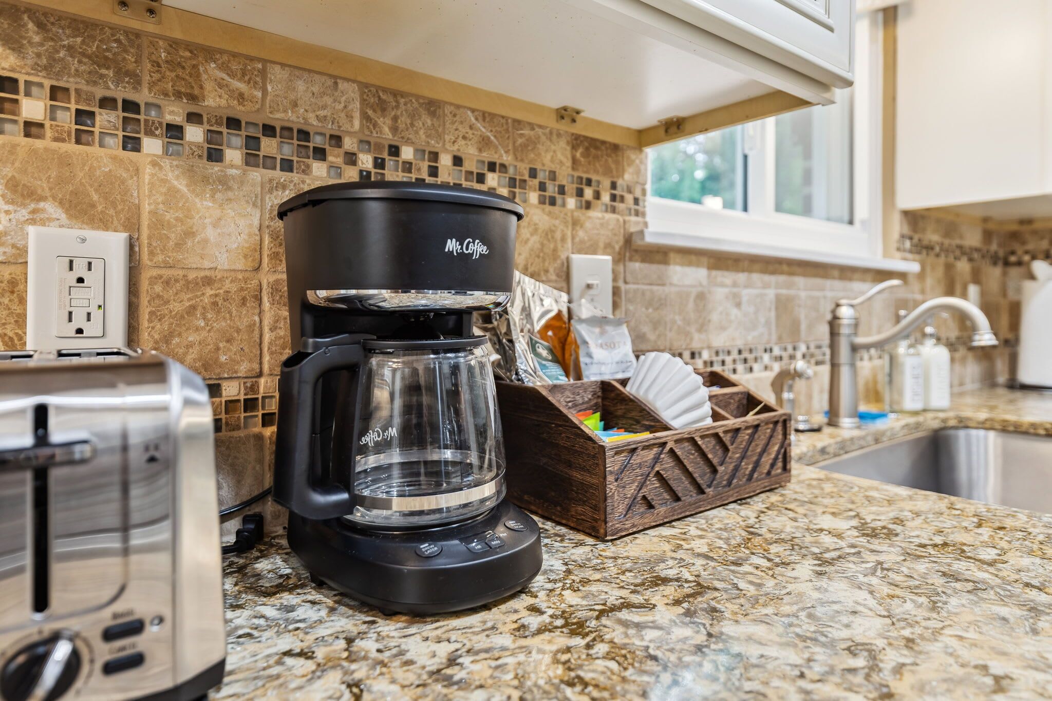 A kitchen with a coffee maker, toaster, and a wooden basket with kitchen utensils.