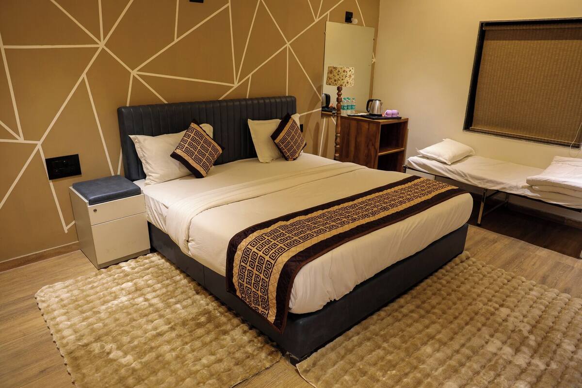 A hotel room with a large bed, bedside tables, a desk, a mirror, and a window with a blind.
