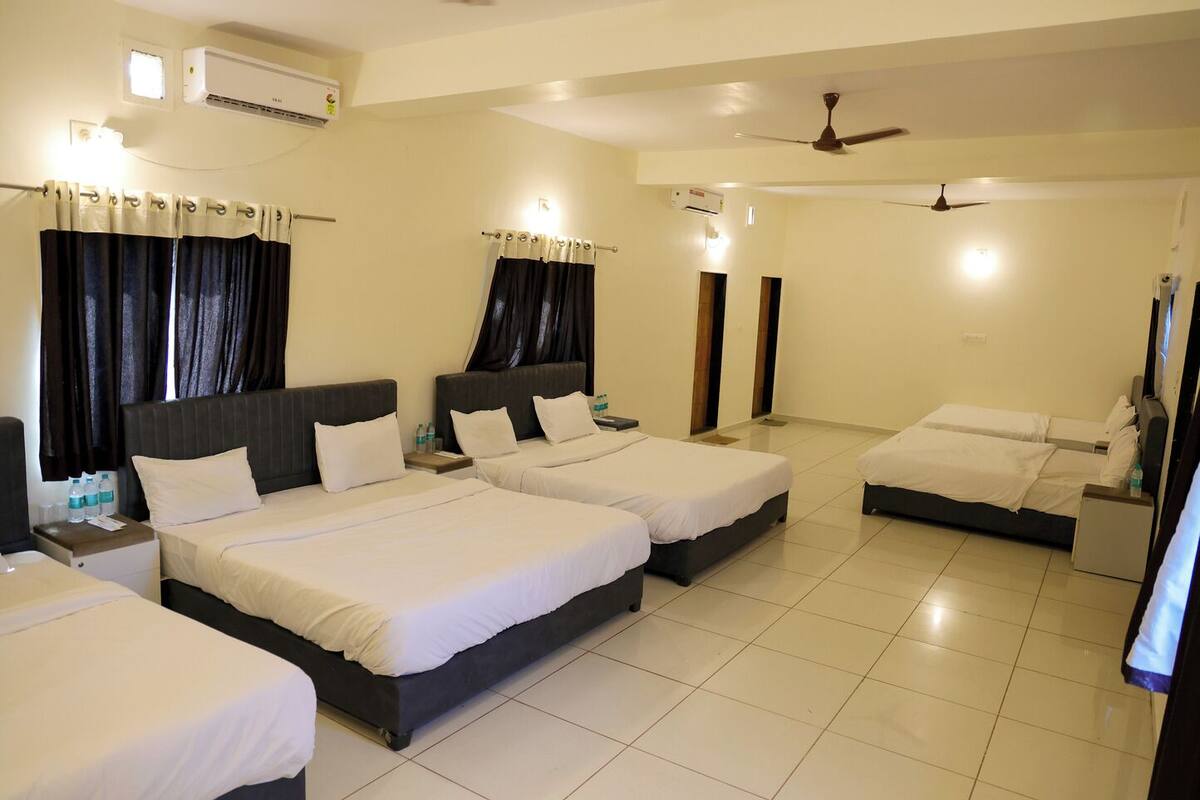 A hotel room with three beds, a ceiling fan, and two air conditioning units.