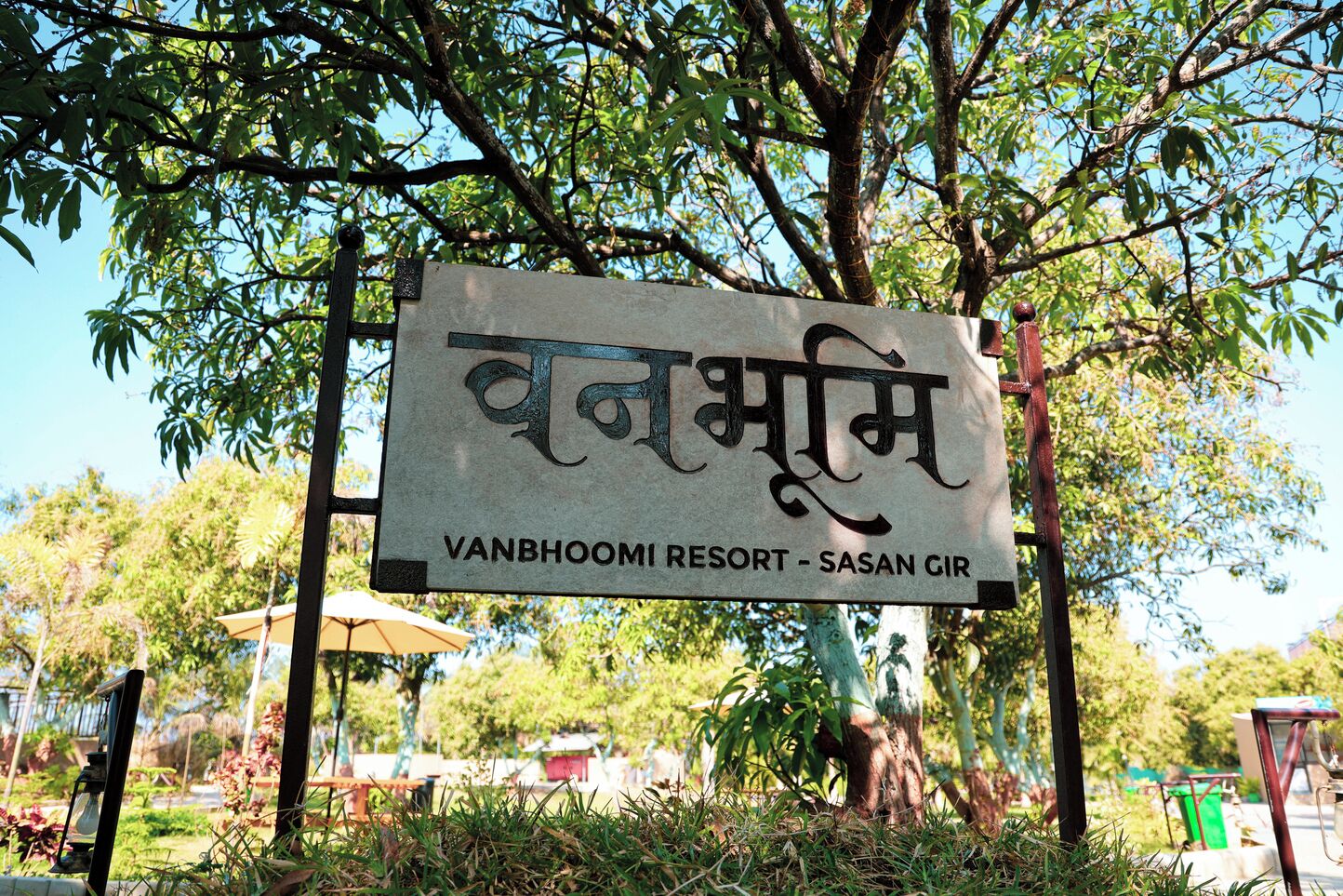 A signboard with text in a non-Latin script, likely Hindi, and English text indicating 'VANBOOMI RESORT - SASAN GIR'.