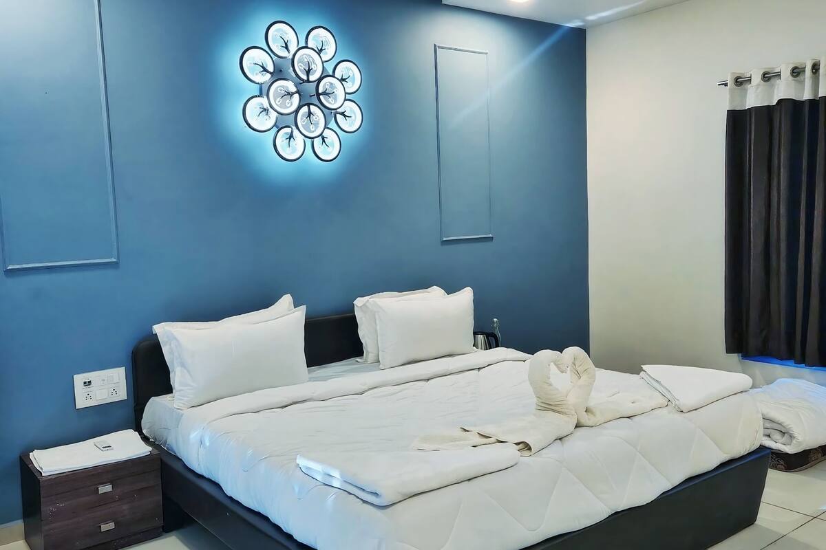 A modern bedroom with a large bed, white bedding, a wall-mounted light fixture, and a power outlet.