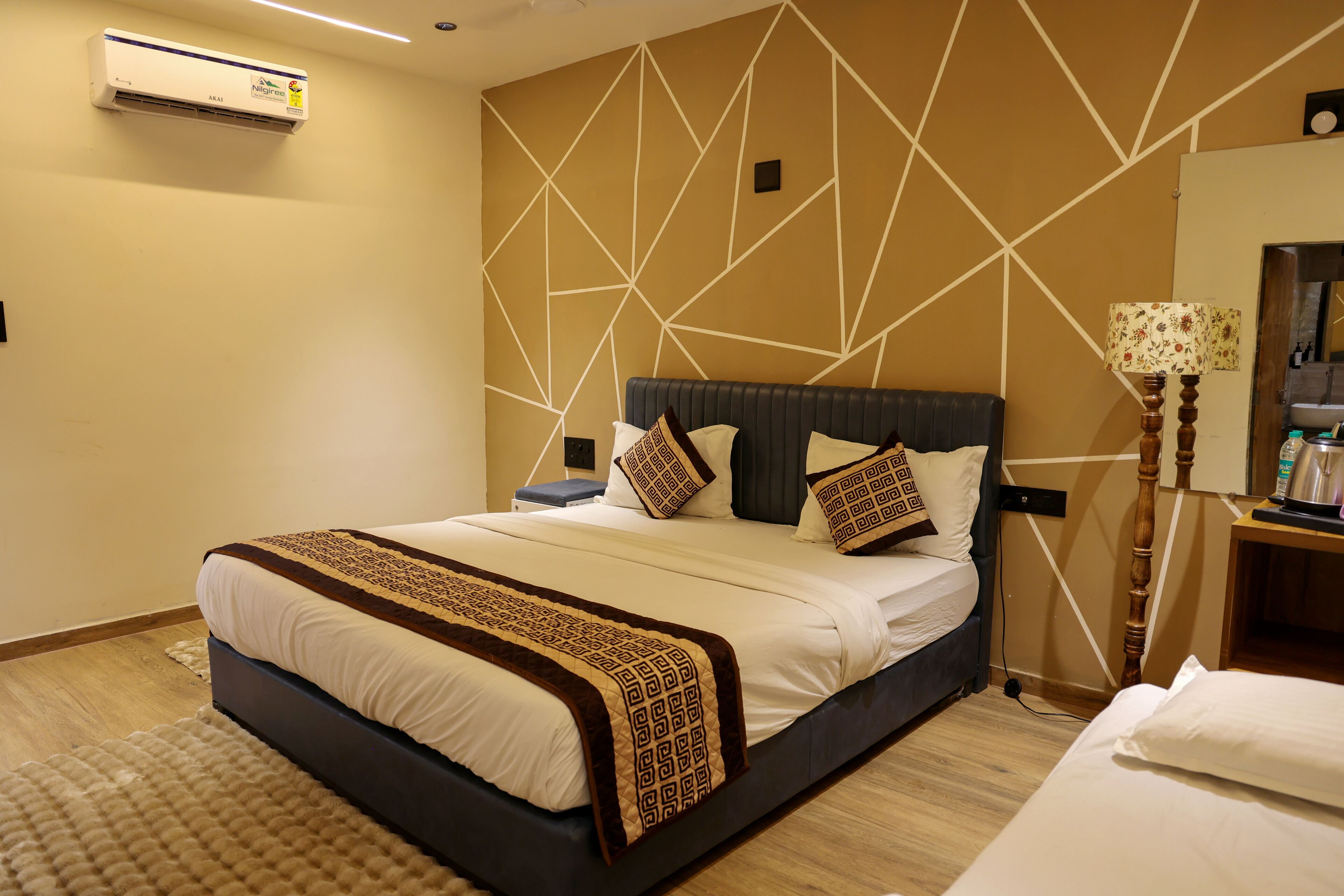 A hotel room with a large bed, a bedside table, a lamp, and a wall-mounted air conditioner.