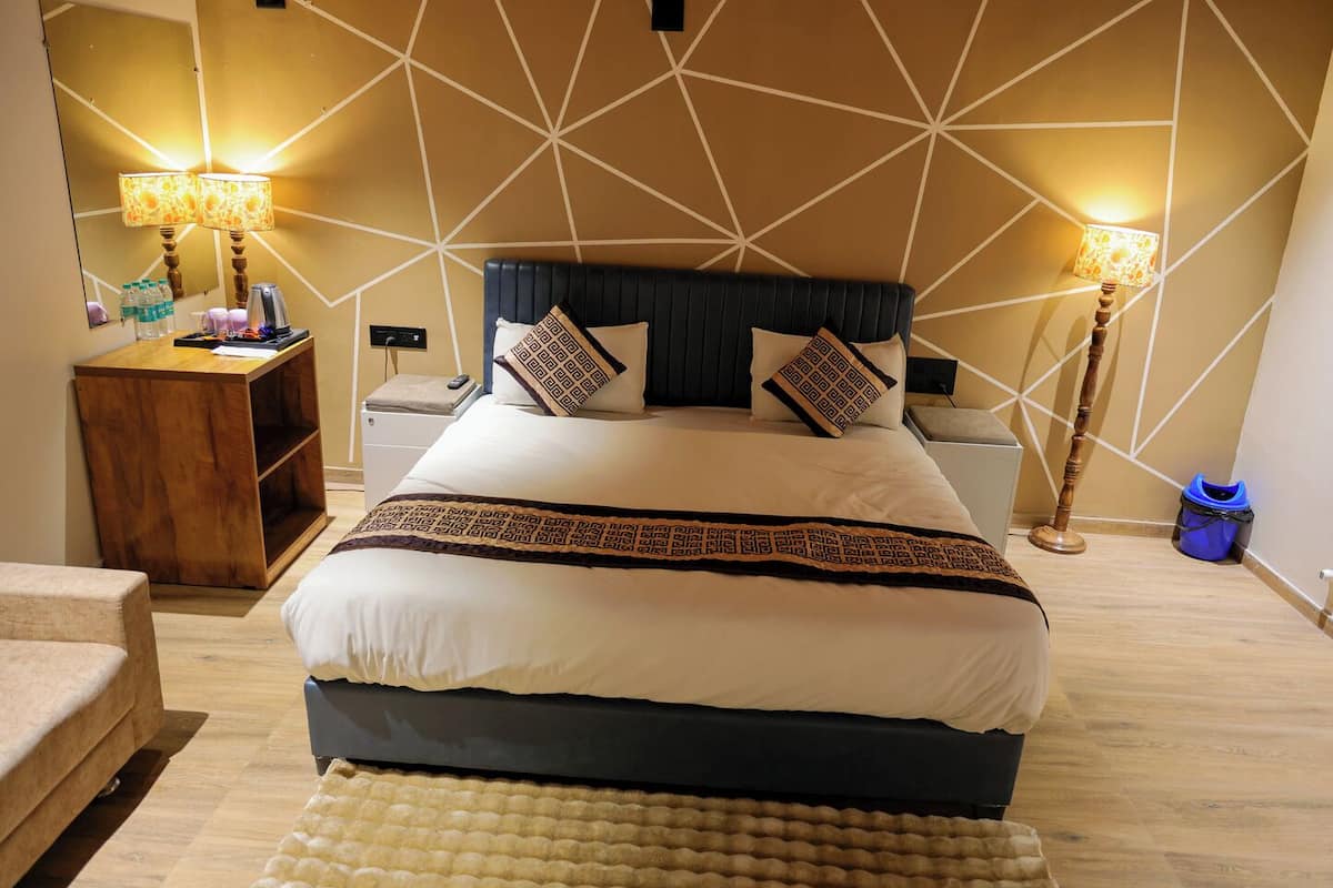 A neatly arranged hotel room with a large bed, bedside tables, a nightstand, a wooden side table, a lamp, and a blue trash bin.