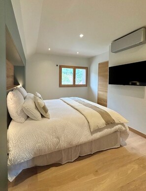 Een slaapkamer met een groot bed, een raam en een wandgemonteerde televisie.