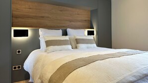 A modern bedroom with a wooden headboard, a large bed with white and beige bedding, and built-in bedside lighting. - Modern duplex with panoramic lake view & 100m from cycle path (Sévrier)