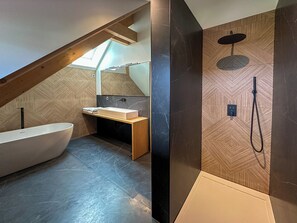 Een moderne badkamer met een vrijstaand bad, een wastafel met spiegel en een douchegedeelte met een handdouche.