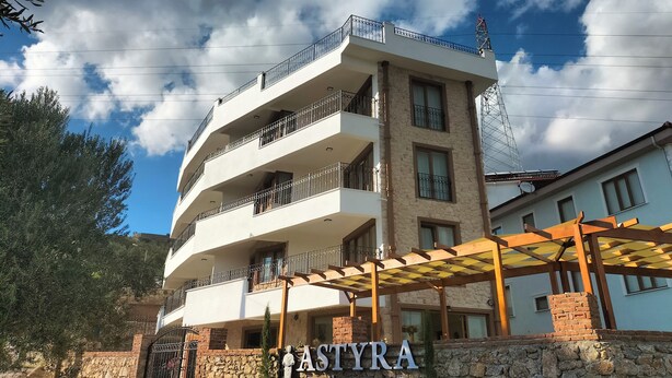 A multi-story building with balconies, a stone wall, and a sign for ASTYRA PANSION & CAFE. - Güre Astyra Pansiyon (Edremit)