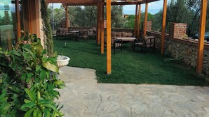 An outdoor patio area with a pergola, stone flooring, and a grassy lawn. - Güre Astyra Pansiyon (Edremit)