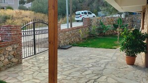 A stone patio with a wooden pergola, a brick wall, and a stone wall with a car parked in the background. - Güre Astyra Pansiyon (Edremit)