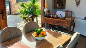A dining area with a table set for four, a bowl of fruit, and a wooden cabinet with decorative items. - Güre Astyra Pansiyon (Edremit)