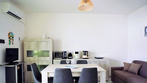 A compact living space with a kitchenette, a dining area with a table and chairs, a sofa, and a television. - Casa Doralucia - Confortevole Casa Vacanze A Santa Maria Di Leuca (Castrignano del Capo)