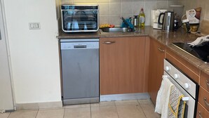 A compact kitchen with wooden cabinets, a built-in microwave, a dishwasher, a coffee maker, and a kettle. - Two Bedroom one Ling Room Apartment (Haifa)