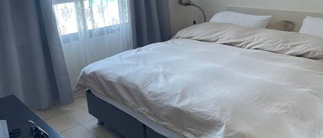 A bedroom with a bed, a desk, and a window with curtains.