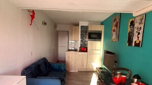 A compact living space with a kitchenette, a blue sofa, and a dining area with red mugs. - Cozy apartment for 2 with WIFI, air conditioning and parking in Cap d'Agde (Cap d'Agde naturisme)