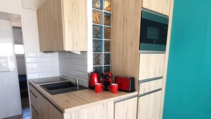 A compact kitchen with wooden cabinets, a black countertop, a red kettle, and a red mug. - Cozy apartment for 2 with WIFI, air conditioning and parking in Cap d'Agde (Cap d'Agde naturisme)