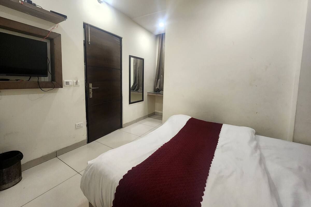 A bedroom with a bed, a door, a mirror, and a television mounted on the wall.