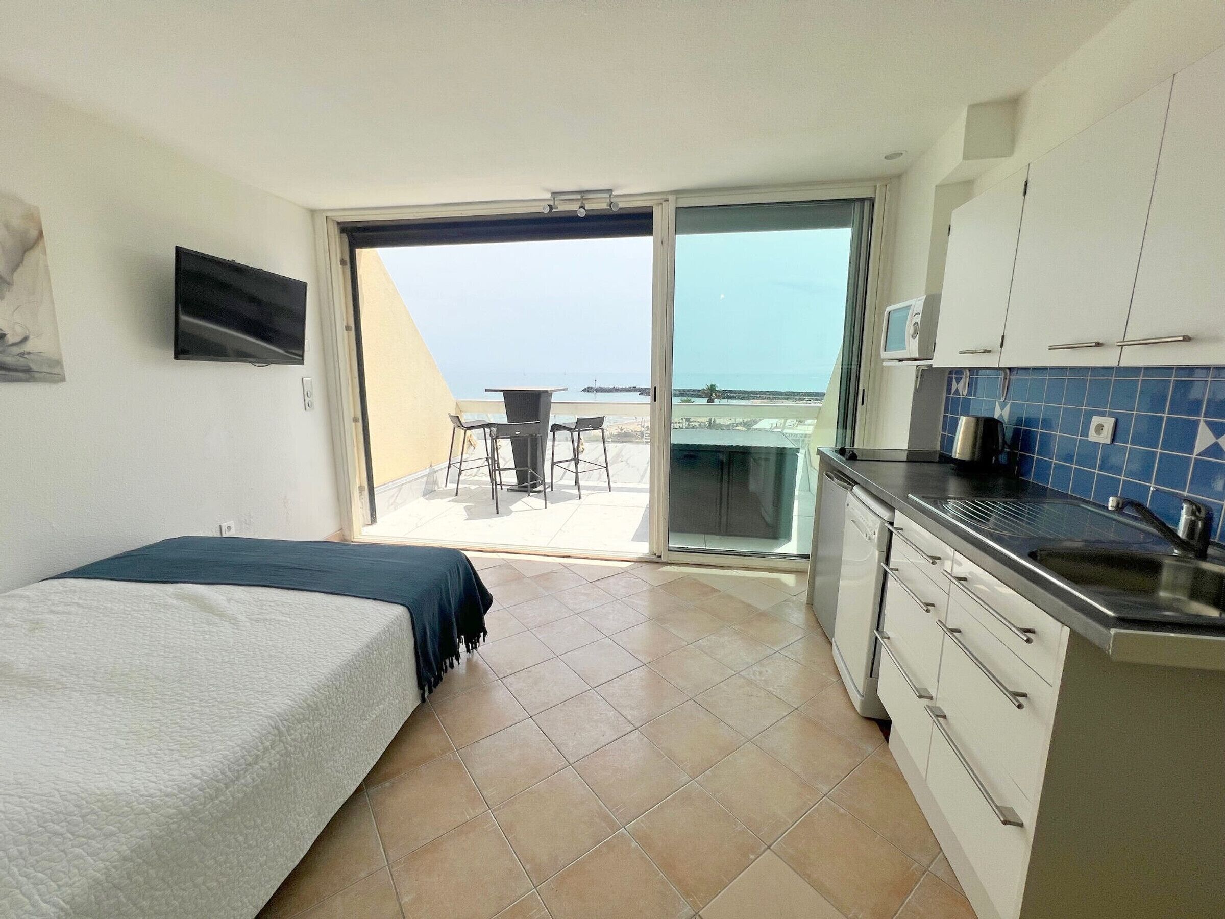Hotelkamer met een bed, kitchenette en balkon met een tafel en stoelen.