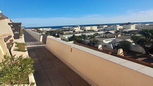 Une terrasse sur le toit offrant une vue sur un quartier résidentiel en bord de mer, avec un toit plat et un ciel dégagé.