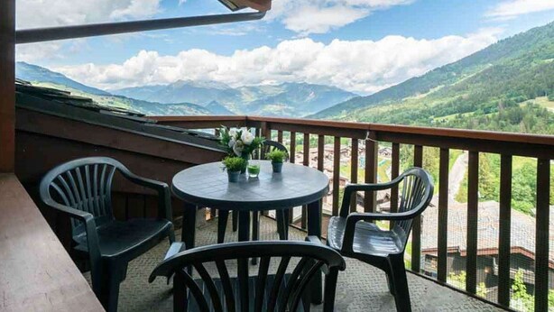 A balcony with a round table and chairs, overlooking a mountainous landscape. - Alpine mezzanine studio, sleeps 4, pets allowed, optional parking (Valmorel)