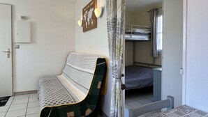 A small, compact room with a bunk bed, a sofa, a world map on the wall, and a door leading to another room.
