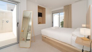 A modern hotel room with a large bed, a bedside table with a lamp, a mirror, a sliding glass door to a balcony, and a shower area. - Villa Santorini (San Fulgencio) (San Fulgencio)