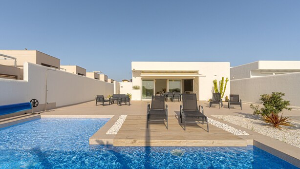 A modern outdoor pool area with a wooden deck, lounge chairs, and a building entrance. - Villa Santorini (San Fulgencio) (San Fulgencio)