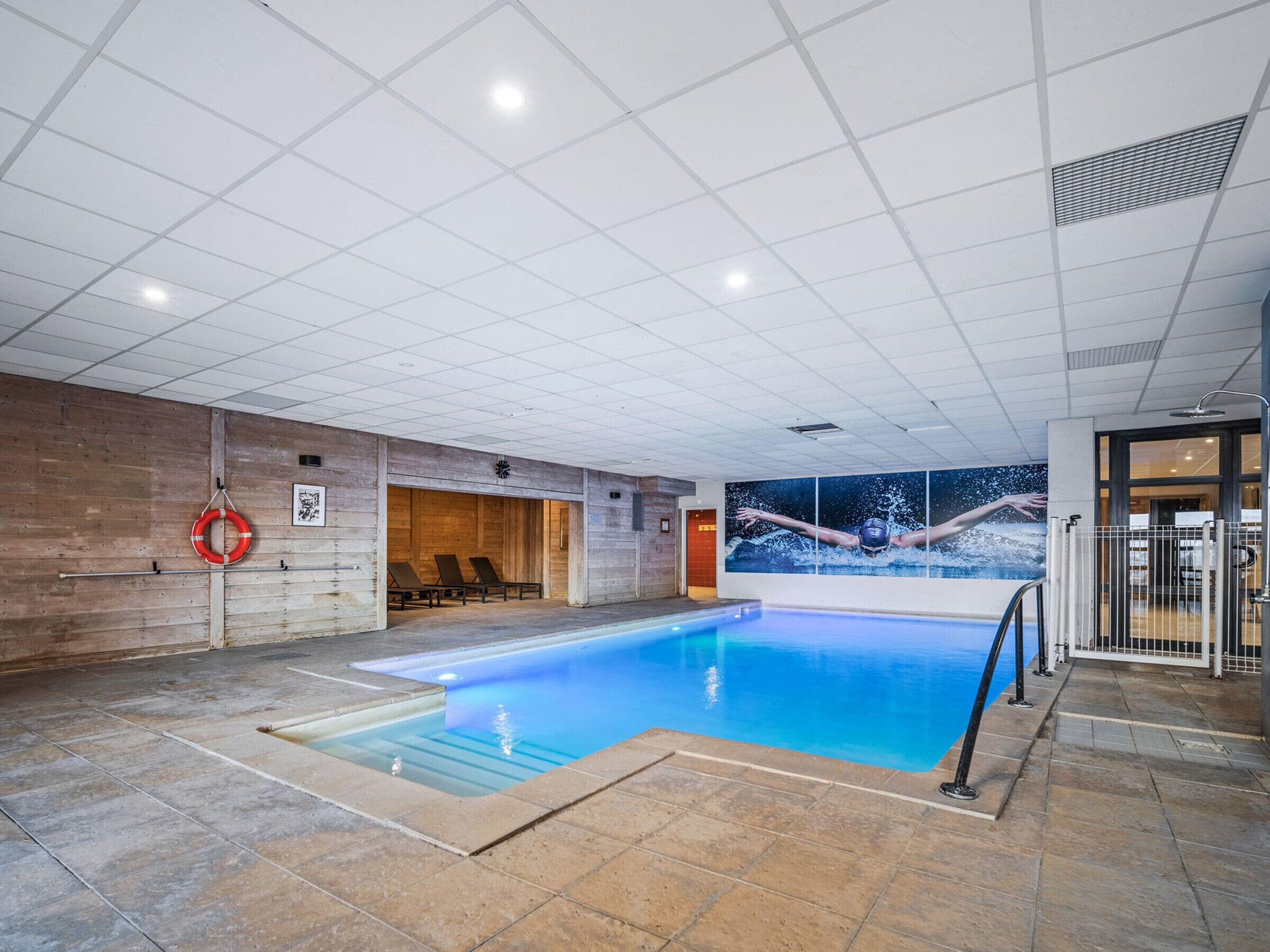 An indoor swimming pool with a tiled floor, a lifebuoy, and a mural of a swimmer.