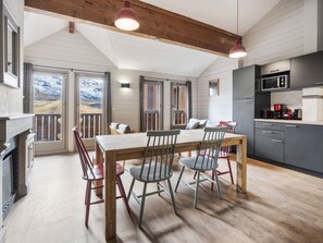 A modern kitchen with a dining area, wooden ceiling beams, and a view of a snowy landscape through the sliding doors. - 62m² Duplex near slopes with wellness area & wifi (Val Thorens)