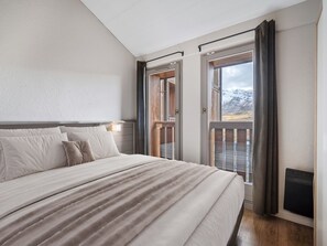 A bedroom with a large bed, a view of mountains through a sliding door, and a wooden deck outside. - 62m² Duplex near slopes with wellness area & wifi (Val Thorens)