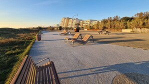 A paved outdoor area with multiple lounge chairs and a wooden bench, surrounded by a low wall and vegetation.