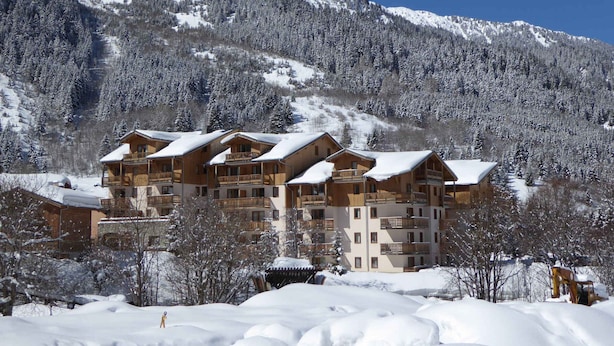 Un chalet à plusieurs étages doté de balcons, entouré de montagnes et d’arbres couverts de neige.