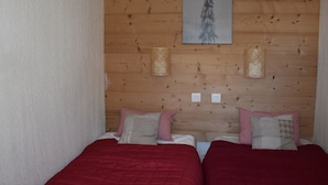 Une pièce aux murs recouverts de lambris en bois, deux lits avec une literie rouge et blanche, une œuvre d’art encadrée au-dessus des lits et deux lampes fixées au mur.