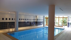 Une piscine intérieure avec des murs carrelés, une eau d’un bleu limpide et quelques chaises.