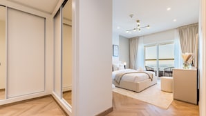 Une chambre moderne avec un grand lit, un bureau et une vue sur la mer grâce à de grandes fenêtres du sol au plafond.