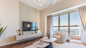 Een moderne woonkamer met een grote flatscreen televisie, een comfortabele bank, een bijzettafeltje en uitzicht op de stad door grote ramen.