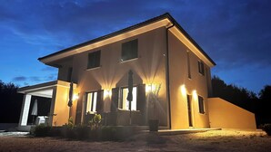 A modern two-story house with a garage, illuminated by exterior lights, surrounded by a landscaped garden. - Apartments Robi 2 (Rovinj)
