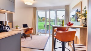 A modern kitchen with a laptop, coffee machine, and a dining area with orange chairs.