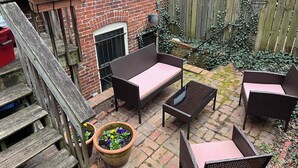 A patio with wicker furniture, a brick wall, a wooden fence, and potted plants. - Capitol Hill & Penn - Steps from Eastern Market (Washington)